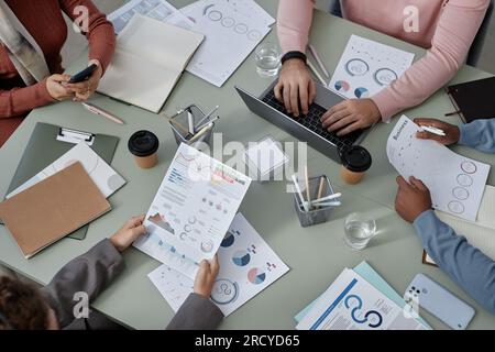 Above angle of hands of young intercultural economists analyzing financial data while one of them typing on laptop keyboard among colleagues Stock Photo