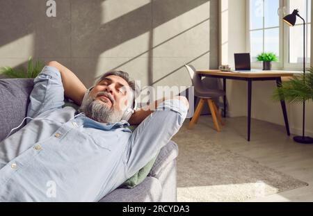 Senior man taking break from work, relaxing on sofa, and listening to music in headphones Stock Photo