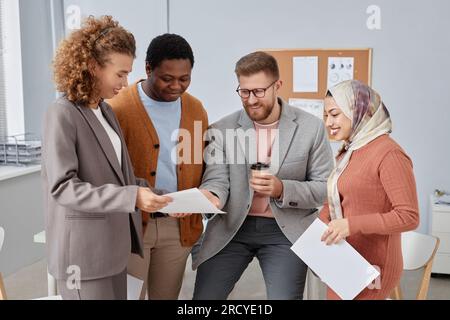 Group of young multicultural economists or analysts discussing data in financial documents at meeting while standing in front of camera Stock Photo