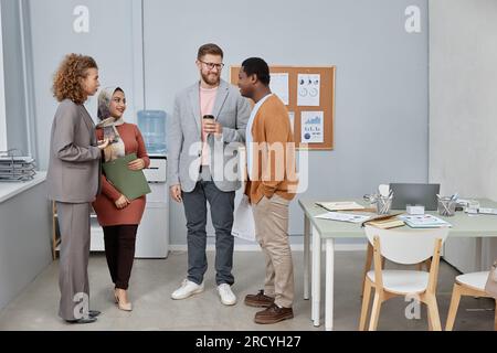 Group of young office managers looking at African American male colleague at coffee break while discussing plans for the evening Stock Photo