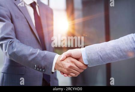Businessmen shake hands, standing near a large office window Stock Photo