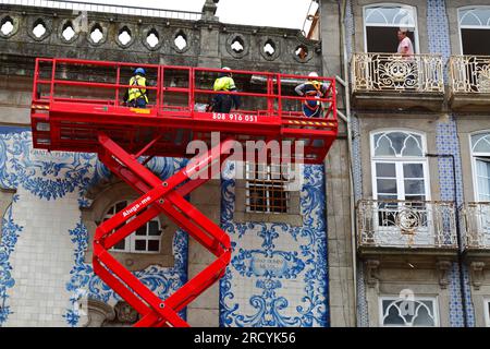 Man on balcony watching workers on raised scissor lift platform doing maintenance inspection of Igreja do Carmo church, Porto / Oporto, Portugal Stock Photo