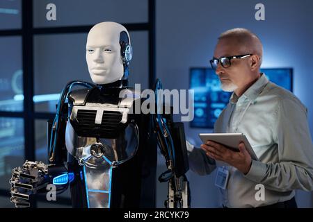 Mature engineer in eyeglasses using tablet pc to connect robot Stock Photo