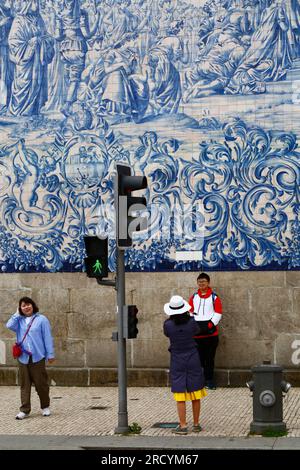 A young male Asian tourist has his photo taken in front of the azulejos / ceramic tiles on the side wall of Igreja do Carmo church, Porto / Oporto, Po Stock Photo