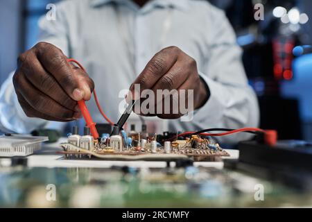 Close-up of African American engineering in white coat soldering motherboard for computer at his workplace in the lab Stock Photo