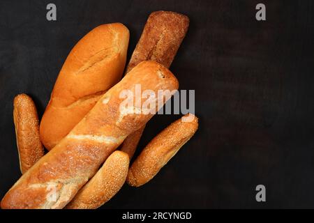 Baguettes, sesame buns and a loaf on a wooden dark table background, top view. Fresh fragrant, crispy pastries Stock Photo