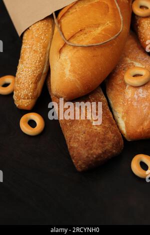 Paper bag with bakery products on a wooden table. Baguettes, sesame buns, long loaf and bagels, fresh fragrant, crispy pastries. Selective focus Stock Photo