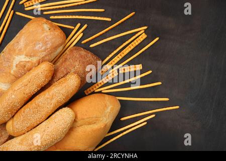 Bakery products on the background of a wooden dark table, top view. Baguettes, long loaf, sesame buns and straw bread. Fresh bakery Stock Photo