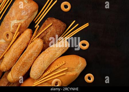 Fresh pastries, bakery products on a wooden table background, top view. Baguettes, long loaf, bagels and sesame buns Stock Photo