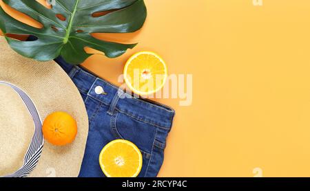 Photo for banners on the theme of vacation, beach and resort. Denim shorts, summer hat, monstera leaf and oranges on orange background, top view, flat Stock Photo