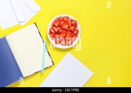 Cozy workspace. Mockup of an open notepad. Top view of a work desk, a notebook for notes, a pen, envelopes and a plate with strawberries on a yellow b Stock Photo