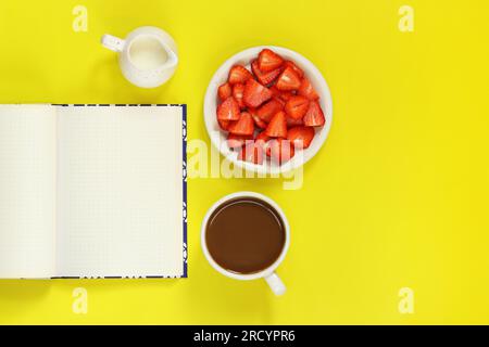 Cozy workspace. Mockup of an open notepad. Top view of a work desk, a notebook for notes, a cup of coffee, a milk jug and a plate with strawberries on Stock Photo