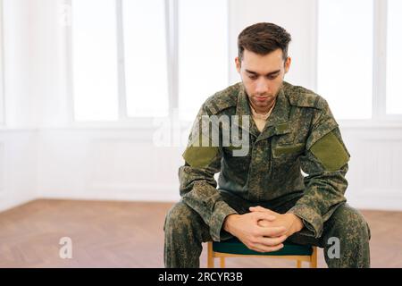 Portrait of frustrated veteran male in camouflage uniform sitting in ...