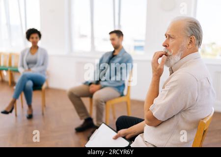 Selective focus of pensive male psychologist having conversation with multiethnic addicted people sitting in circle during therapy session. Stock Photo