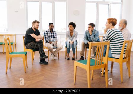 Portrait of group therapy session with diverse people sharing problems and stories during psychotherapy session. Multi-ethnic men and women sitting in Stock Photo