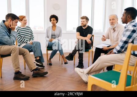 Rear view of thoughtful young woman thinking about mental problem or addiction sitting in circle during group therapy session. Concept of mental Stock Photo