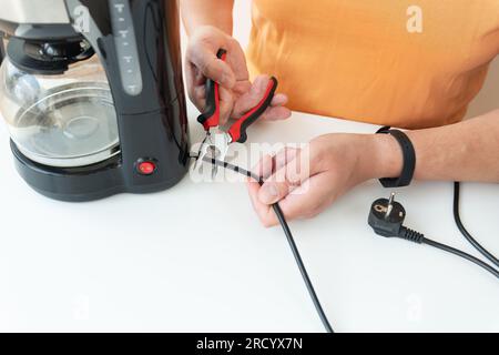 A man is sitting at a table, repairing a small coffee maker with a screwdriver. Close-up Stock Photo