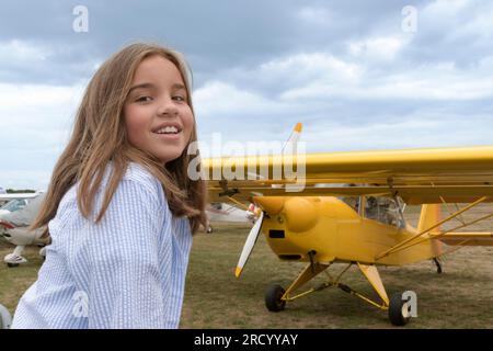 Smiling teenage girl in front of a vintage yellow plane on the airfield Stock Photo