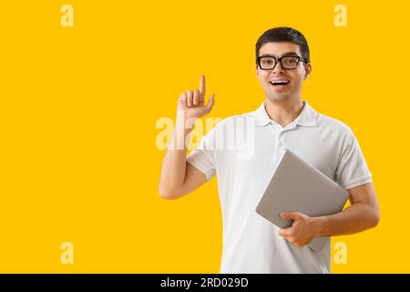 Male programmer with laptop pointing at something on yellow background Stock Photo