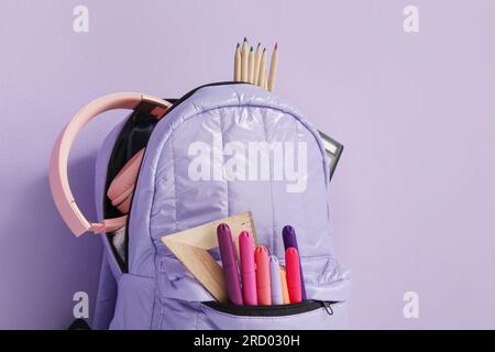 School backpack with different stationery and headphones on purple background Stock Photo