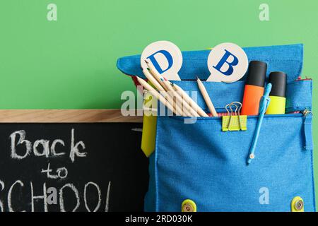 School backpack, different stationery and blackboard with text BACK TO SCHOOL on green background Stock Photo