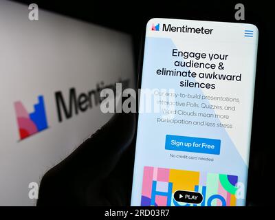 Person holding smartphone with webpage of presentation software company Mentimeter on screen in front of logo. Focus on center of phone display. Stock Photo