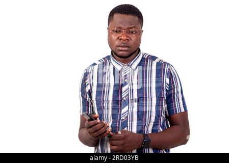 a young man in shirt standing on white background holding cellphone while thinking. Stock Photo