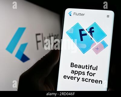 Person holding cellphone with website of UI software development kit Flutter (Google) on screen with logo. Focus on center of phone display. Stock Photo