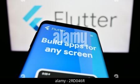 Smartphone with webpage of UI software development kit Flutter (Google) on screen in front of logo. Focus on top-left of phone display. Stock Photo