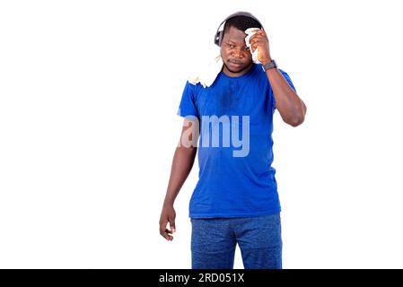 young man standing in a room wiping off sweat with a towel and listening to music through headphones. Stock Photo