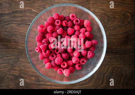 Overhead view of a glass bowl filled with red raspberries on a wood table Stock Photo