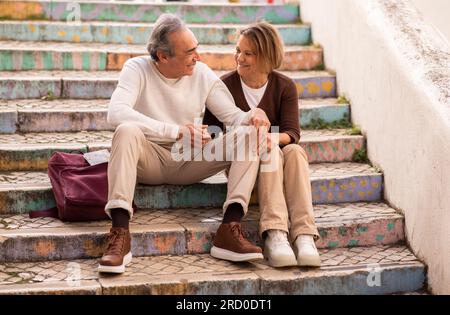 Mature Man And Woman With Backpack Sitting On Steps Outdoors Stock Photo