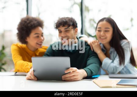 Diverse university student friends, using tablet, studying, learning and discussing research in college classroom Stock Photo