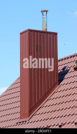 A chimney on the roof of a house covered with metal tiles or a metal profile Stock Photo