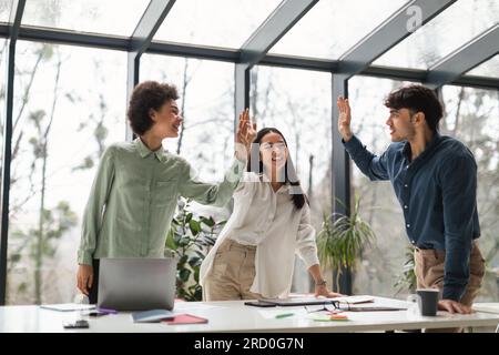 Multicultural Colleagues Team Celebrates Achievement with High Five In Office Stock Photo