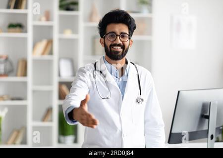 Friendly handsome middle eastern doctor outstretching hand and smiling Stock Photo