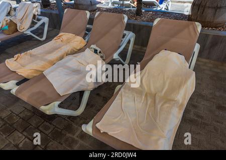 Close-up view of sun loungers with wet towels near outdoor pool in hotel. Spain. Stock Photo