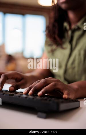 Closeup of african american student writing homework using computer keyboard while studying remote from home living room. Selective focus on woman freelancer hands typing text while chatting. Stock Photo