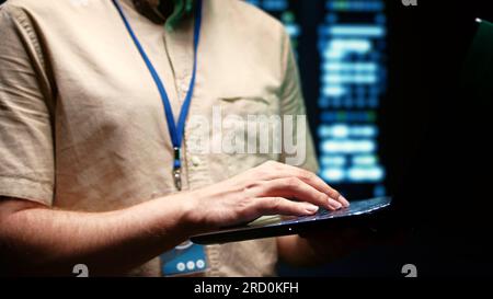 Close up of system administrator using laptop to check operational server clusters. Rackmounts in computer network security data center providing processing and memory resources for several workloads Stock Photo