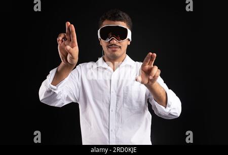 Latin man experiencing virtual reality in modern vision pro vr glasses, interacting with virtual screens gesturing hands Stock Photo