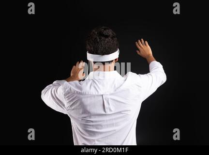Back view of man touching invisible screen while experiencing cyberspace in vision pro VR glasses, black background Stock Photo