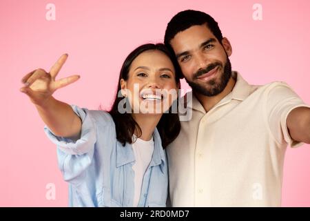 Beautiful cute multiracial young couple taking selfie on pink background Stock Photo
