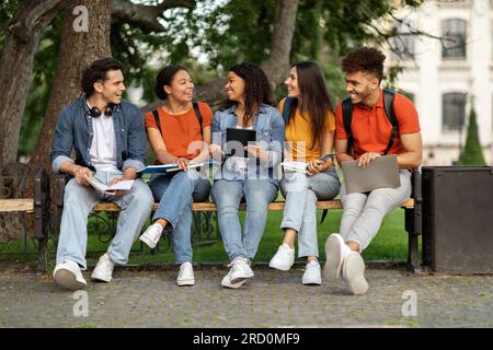Diverse students friends sitting on bench outdoors in university campus Stock Photo