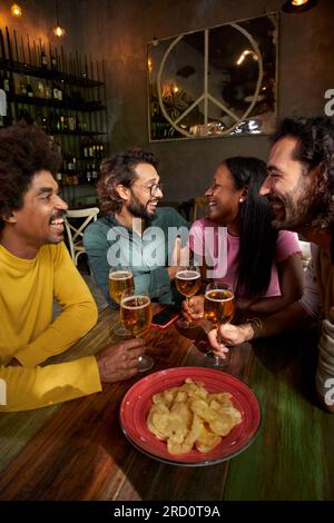 Young people laughing and drinking in a pub. Group of friends celebrating a party together Stock Photo