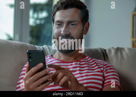 Man using smartphone with facial recognition system at home. Security application scanning his face for approving owner's identity Stock Photo