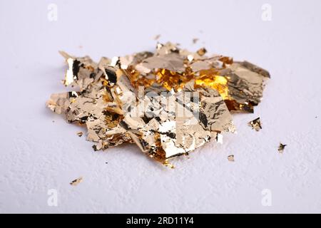 Many pieces of edible gold leaf on white textured table, closeup Stock Photo