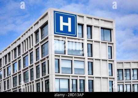 Modern concrete building with large blue H sign for hospital Stock Photo