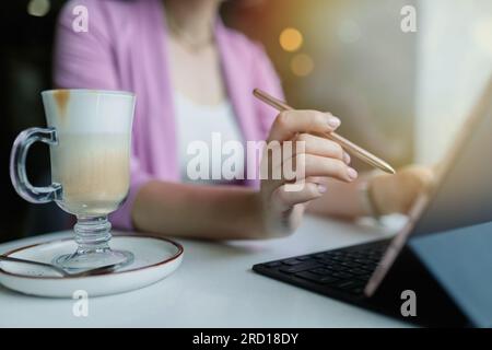 Stylus from a tablet in a woman's hand in front of a tablet on a table in a coffee shop. Young woman draws on a tablet Stock Photo