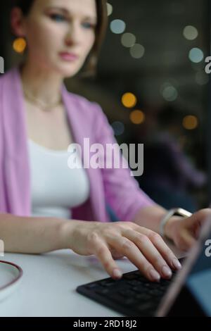 Young businesswoman working on a laptop in a cafe, freelance work concept, focus on her hands, vertical Stock Photo