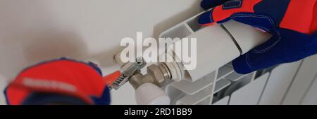 Gloved craftsman installs heating battery in house. Stock Photo